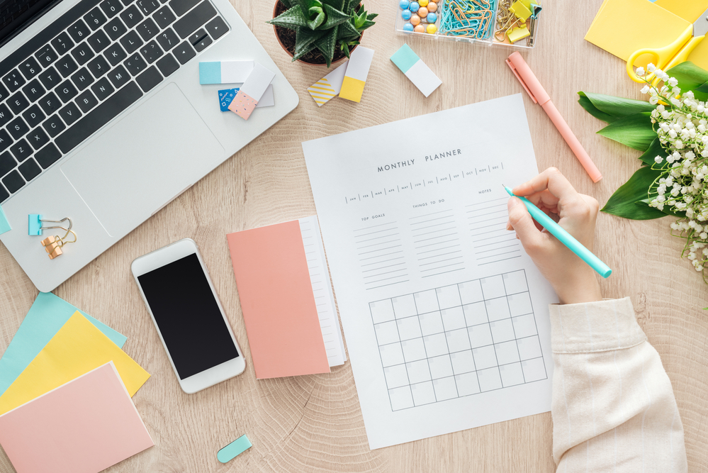 Desk with items on top woman's hand writing on a sheet of paper